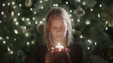 el niño mira la vela encendida en sus manos. con el telón de fondo de las luces borrosas del árbol de navidad. pide un deseo