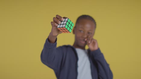 studio portrait of young boy on asd spectrum solving puzzle cube on yellow background 3