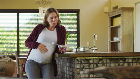 caucasian pregnant woman sitting in kitchen and eating ice cream