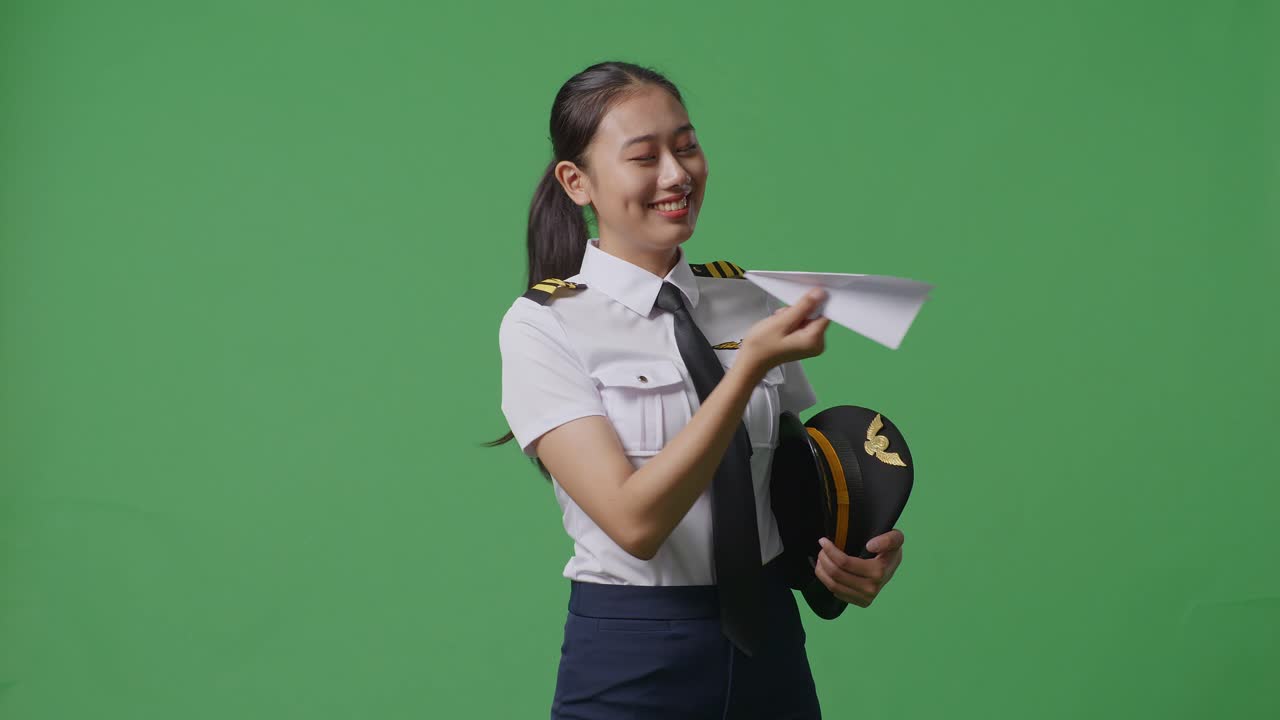 프로 유니폼을 입은 아시아 여성 조종사가 종이 비행기를 발사하고, 제트 모델을 손에 들고, 항공 아카데미 조종사, 녹색 스크린 배경 스튜디오에서 항공기 선장