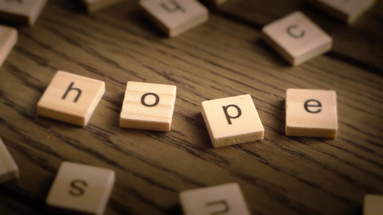 Wooden tiles spell the word hope as the camera pans gently across a rustic wooden surface in warm lighting.