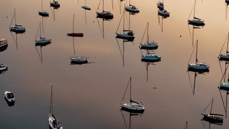 aerial forward shot of sailboats on still windermere lake reflecting fiery sunrise