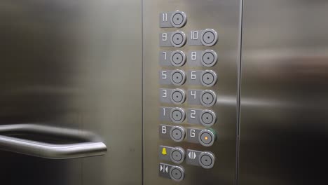 Mano-Femenina-Presionando-El-Botón-De-La-Planta-Baja-En-Un-Ascensor