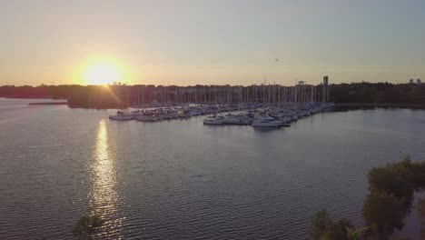 a tomada aérea do pôr-do-sol do veleiro marina yacht club dock na baía do lago entre árvores verdes e pássaros com edifícios da cidade horizonte no fundo em toronto, ontário, canadá