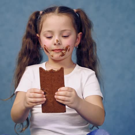 dirty girl eating chocolate. funny child holding a bar of chocolate and biting a piece of sweet isolated in studio. joyful childhood.
