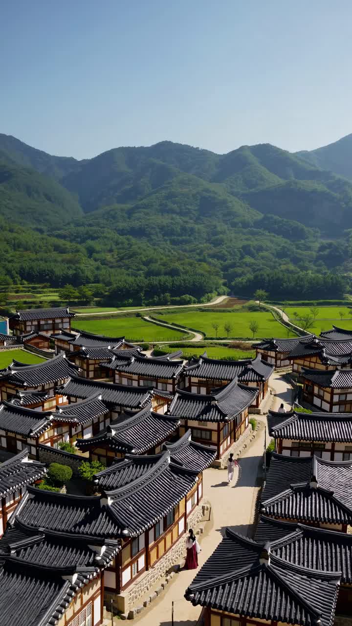 Video aereo che riprende un villaggio tradizionale coreano con tetti di tegole, sullo sfondo di lussureggianti montagne verdi