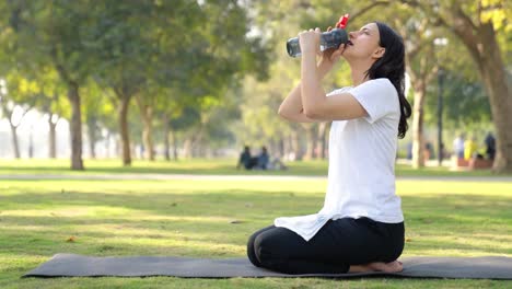 Chica-India-De-Yoga-Bebiendo-Agua-De-Una-Botella-De-Sorbete-En-Un-Parque-Por-La-Mañana