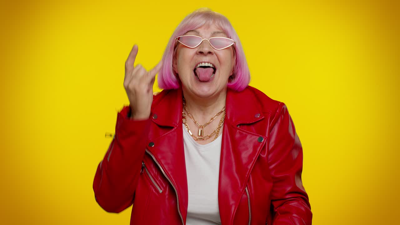 Anziana donna gioiosa ed euforica che mostra il gesto del rock 'n' roll con le mani, un segno "cool", e balla