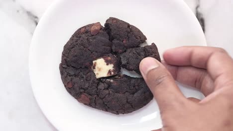 la mano recogiendo un pedazo de galleta de chispas de chocolate rotas con relleno de chocolate blanco