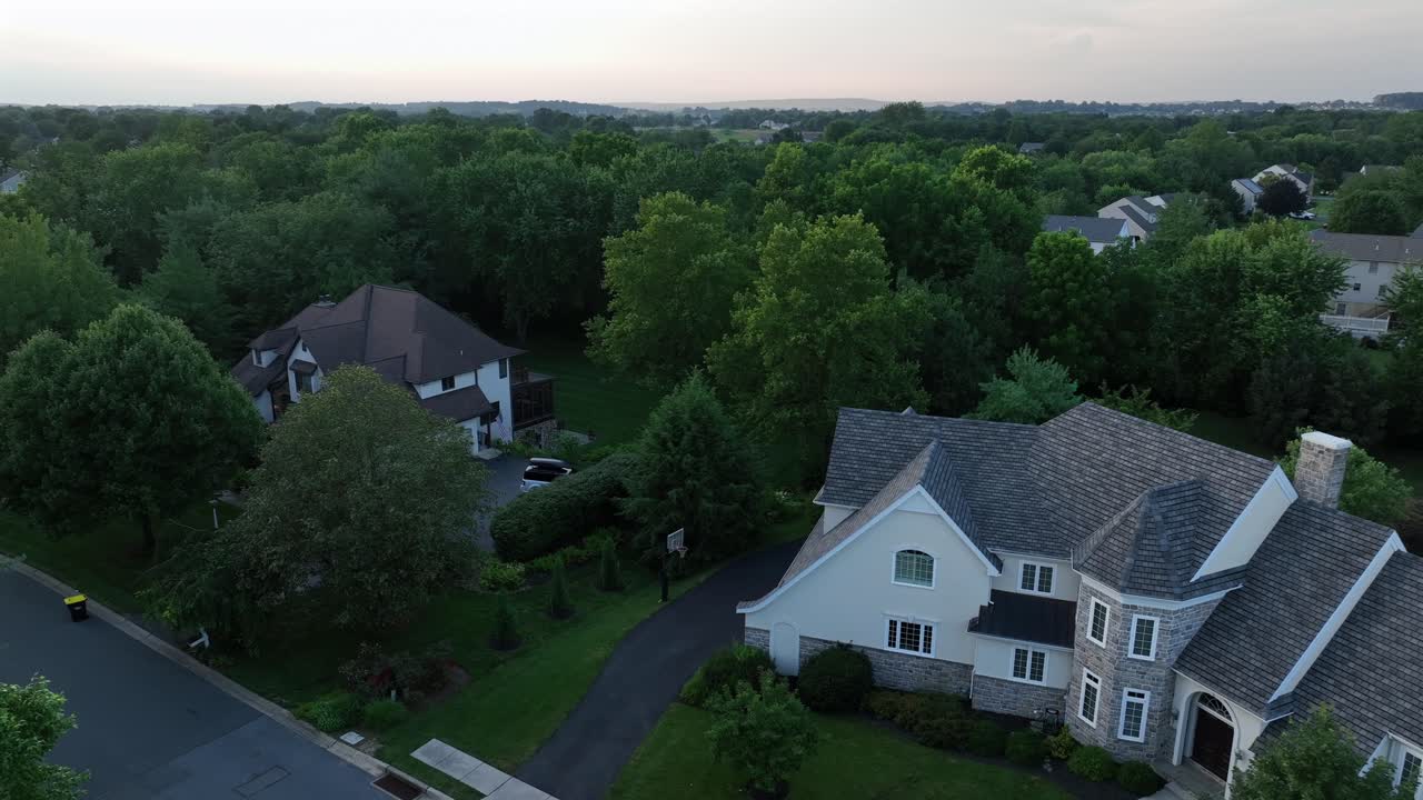 Upscale American suburb area. Large two-story homes with pitched roofs, stone and siding facades , surrounded by trees and winding roads in peaceful residential neighborhood. Aerial view at dusk