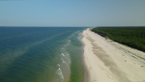 Flying-forward-along-the-white-sand-beach-line-in-Osetnik,-Poland,-daytime-cloudless-sky