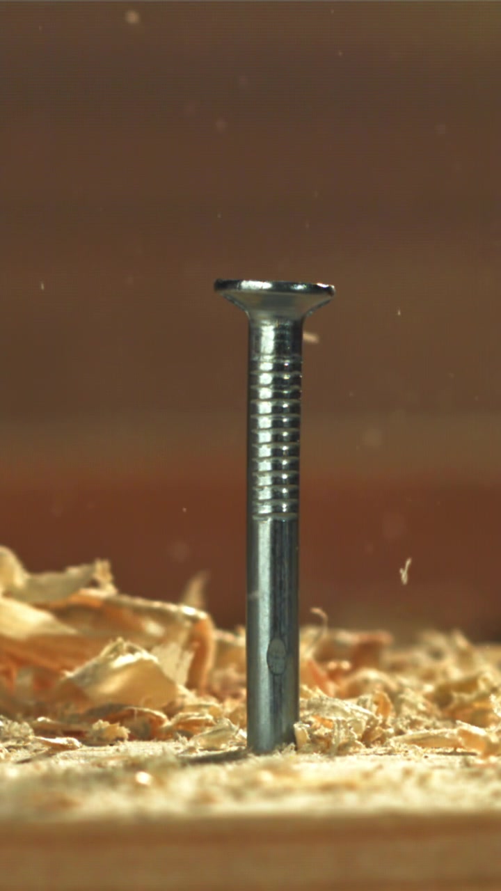 Close-up of a metal nail hammered into wood with sawdust