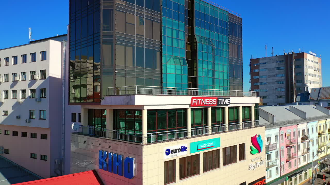 Approaching glassy multi-storied building of a business centre. Drone rising above downtown.
