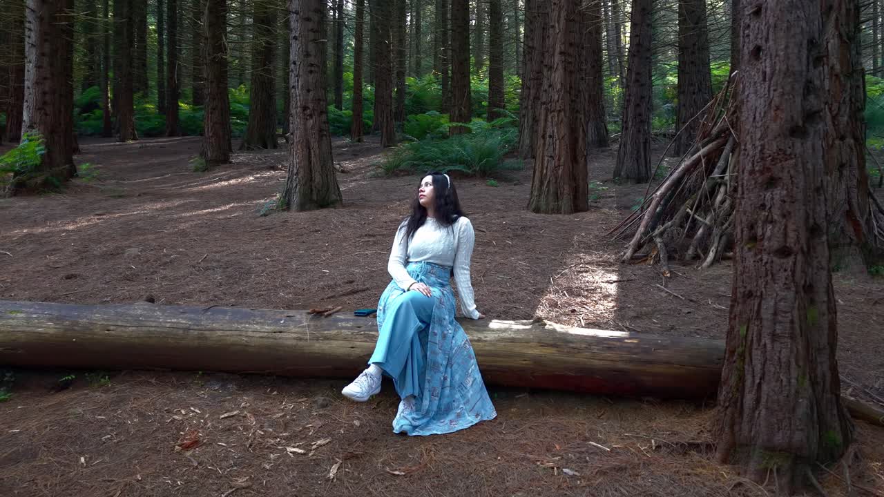 A serene scene in Melbourne's Woolrich Forest Park shows a woman peacefully seated on a log amidst tall trees. Sunlight filters through the canopy, creating a tranquil setting