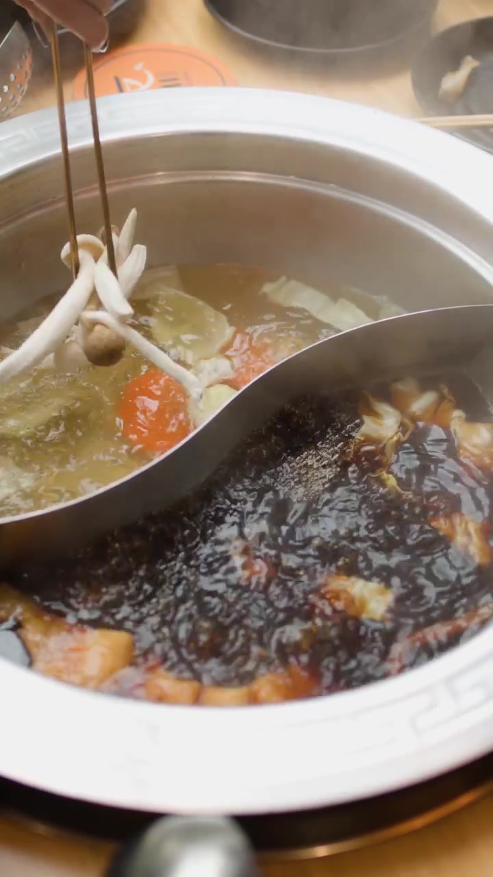 Le bacchette aggiungono verdure e carne affettata a un hot pot fumante con doppio brodo al tavolo da pranzo.