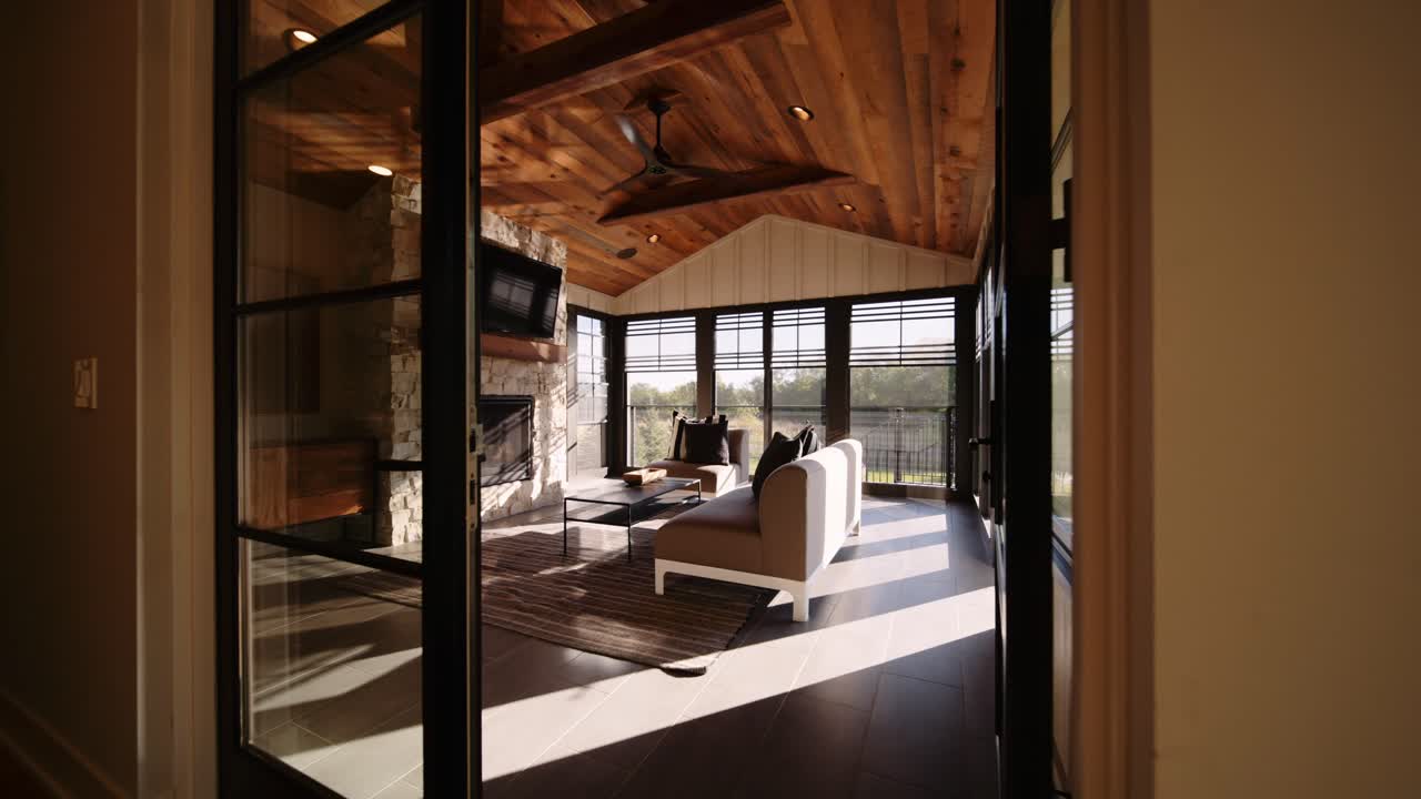 A rustic-style sun room featuring a wooden ceiling, stone fireplace, and large windows, creating a warm, inviting space with natural light streaming in