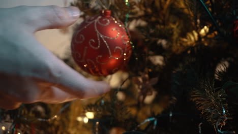 hand putting gold and red ball on christmas tree