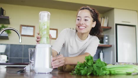 happy biracial woman using blender, preparing smoothie in kitchen