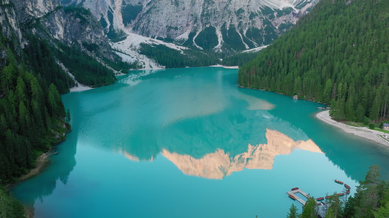 Panoramic drone shot of Lago di Braies at sunrise, with glass-like waters mirroring the surrounding Dolomite peaks under a crystal-clear sky