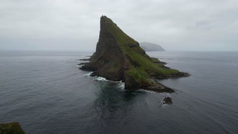 Aerial-wide-shot-of-Tindholmur-Island-with-dense-grey-clouds-at-sky-over-Atlantic-Ocean-on-Faroe-Islands