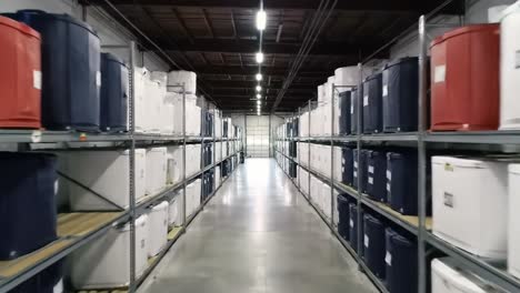 a spacious warehouse aisle with storage containers aligned on shelves, showcasing a neatly organized display of various colored containers under bright industrial lighting
