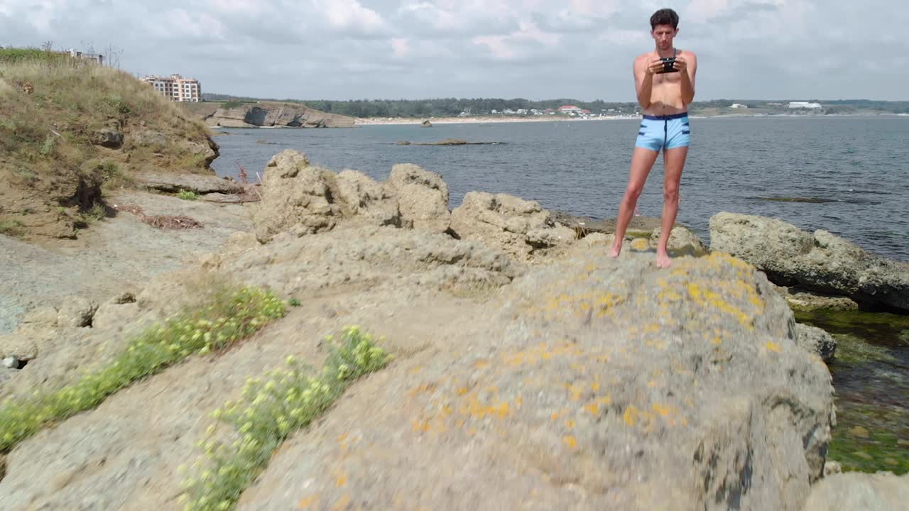 Aerial low selfie shot of drone pilot stay on big sea cliff in summer sunny day