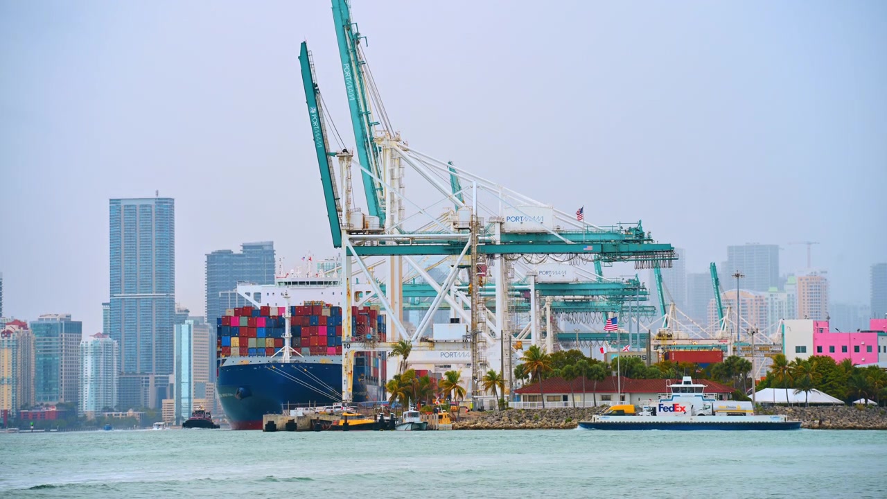 Miami, USA, 16 April 2026: Cargo container ship and cranes at PortMiami terminal. Large industrial container ship docked next to teal cranes at PortMiami with a FedEx vessel in the water.