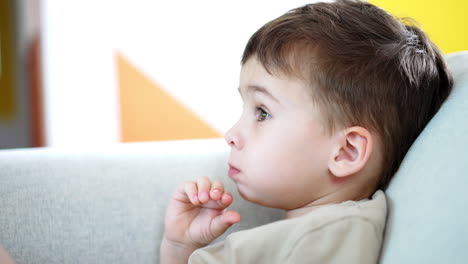 young child enjoys snack while relaxing. a child sits comfortably on a sofa, quietly enjoying a snack and watching something off-screen