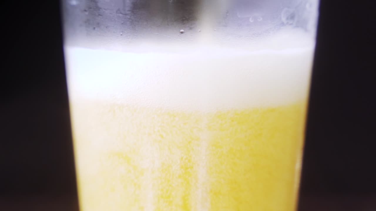 Close up shot of a beer being poured into a empty glass in slow motion