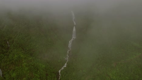 Aerial-of-waterfall-cascading-down-a-lush,-fog-covered-mountain-in-Sapa,-Vietnam