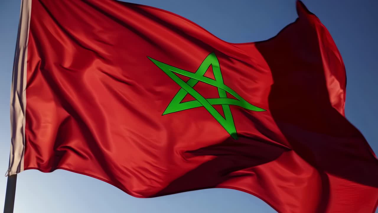 Low-angle video shot of a red flag waving against a clear blue sky, capturing movement and vibrancy