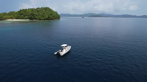 flying around a dhingy parked next to beautiful green island with white sandy beach in raja ampat, indonesia, papua