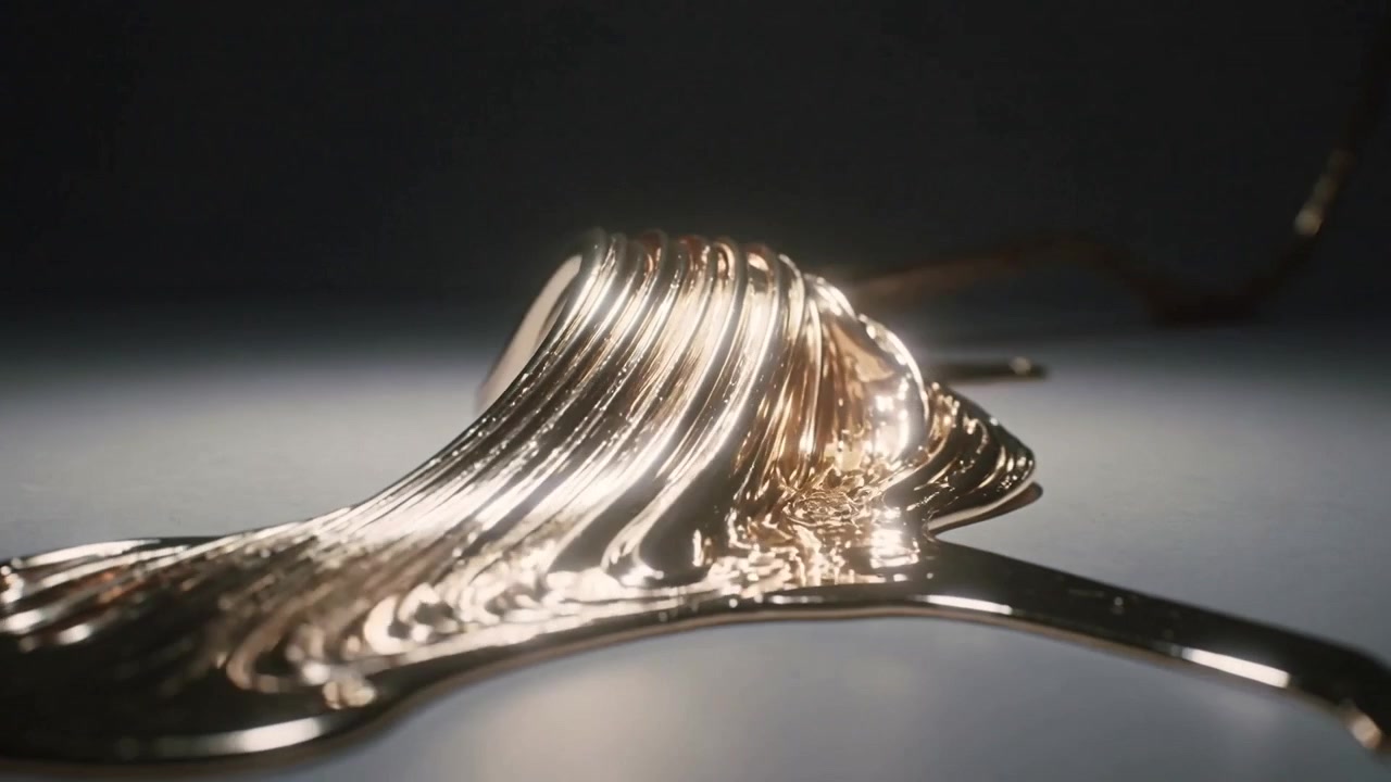 Ein herabfallendes Goldband windet sich nach rechts, schält sich ab und breitet sich zu einem dünnen Blatt auf einer grauen Oberfläche aus.