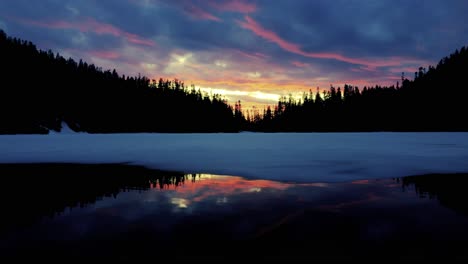 Stunning-drone-shot-of-a-cotton-candy-sunset-over-top-a-frozen-lake-with-the-reflection-in-the-water