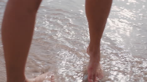 Cerrar-Los-Pies-De-Una-Mujer-Caminando-Descalzo-En-La-Playa-Disfrutando-De-Las-Olas-Salpicando-Suavemente-A-Una-Turista-En-Vacaciones-De-Verano