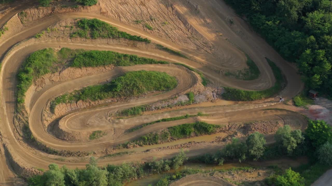 High-angle drone view of winding dirt motocross track cutting through forested landscape