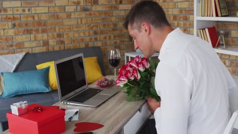 Caucasian-man-making-video-call-using-laptop-holding-bunch-of-flowers-and-blowing-kiss