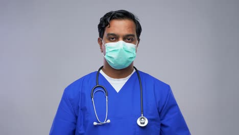 Indian-Male-Doctor-in-Mask-Putting-on-Goggles.healthcare,-profession-and-medicine-concept-indian-doctor-or-male-nurse-in-blue-uniform-and-face-protective-medical-mask-for-protection-from-virus-disease-putting-goggles-on-over-grey-background