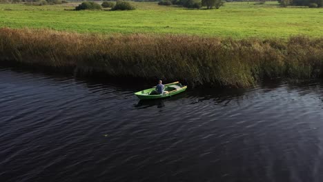 Circulating-drone-shot-with-man-on-fishing-boat-who-are-fishing-in-the-river-near-reeds