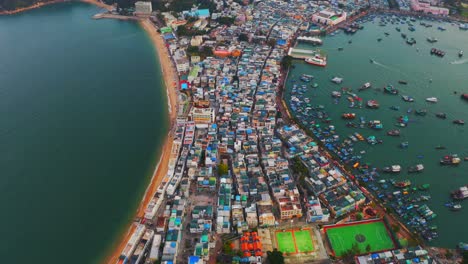 Drone-shot-traveling-forward-of-a-city-built-on-an-isthmus-with-an-harbor-and-a-popular-beach-during-the-day