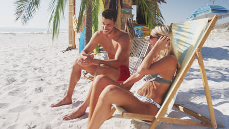 Caucasian-couple-sitting-on-sunbeds-on-the-beach