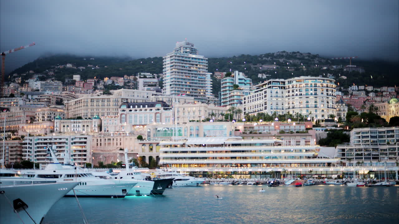 Boats docked in the Monaco Marina with the skyline of the city on the background in the evening
