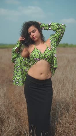 young woman posing in dry grass field, wearing green crop top and black skirt