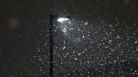 large snow flakes rapidly falling during a blizzard near a street lamp in slow motion