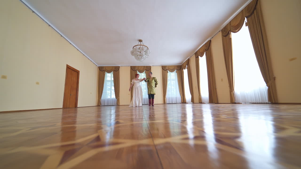 Approaching the adult couple dancing in the large ball room. Aging people in historic costumes perform old-fashioned dance. Low angle view.