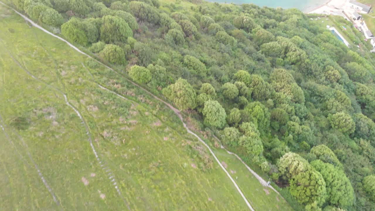un avance aéreo revela imágenes de la bahía de lulworth con playa de arena, agua azul cristalino, barco de pesca, kayakistas y olas que se estrellan en el acantilado rocoso