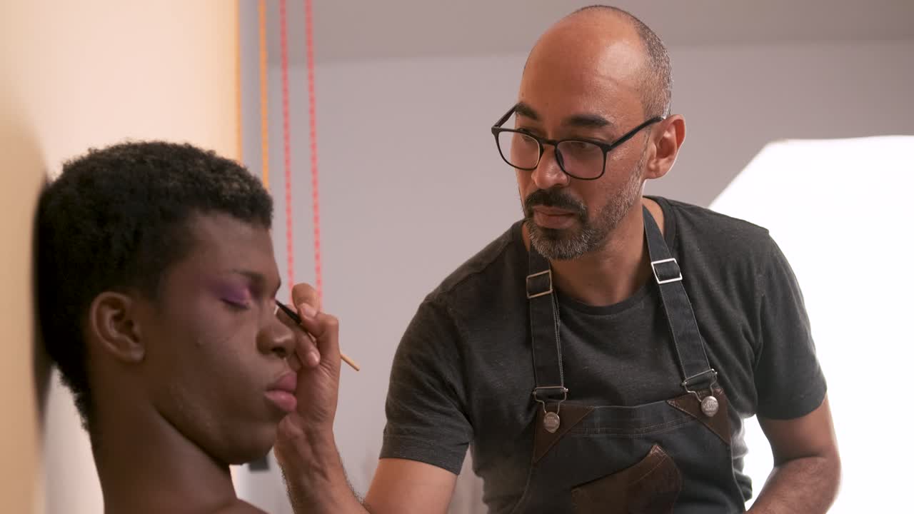 Male makeup artist doing makeup on an African transgender person.