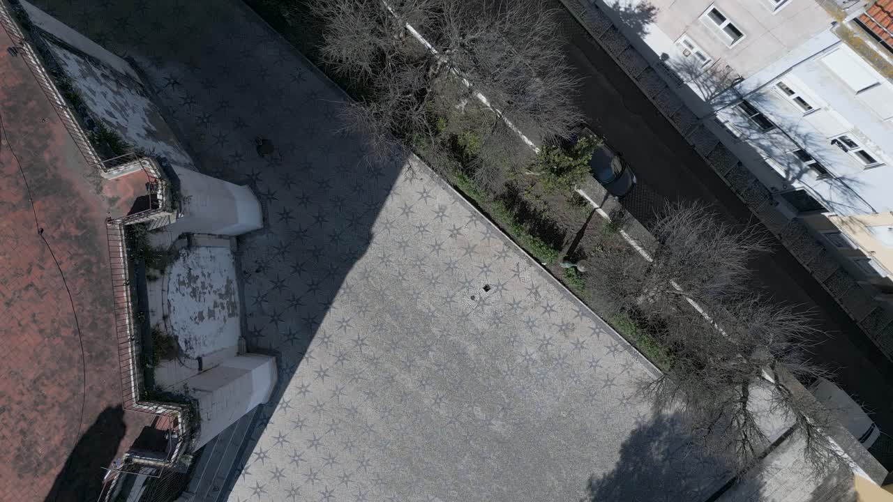 Veduta aerea a volo d'uccello su una zona residenziale con edifici lungo la strada, auto parcheggiate e una fila di alberi.