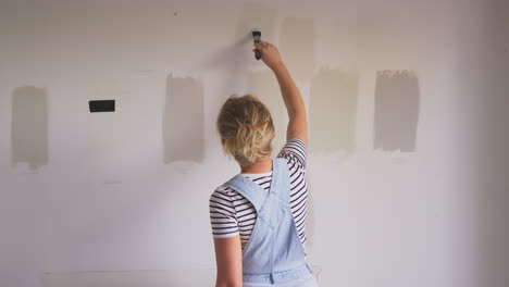 rear view of woman decorating room in house painting tester paint colour strips on wall