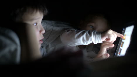 dos niños pequeños tratan de ver la película por la noche usando la tableta